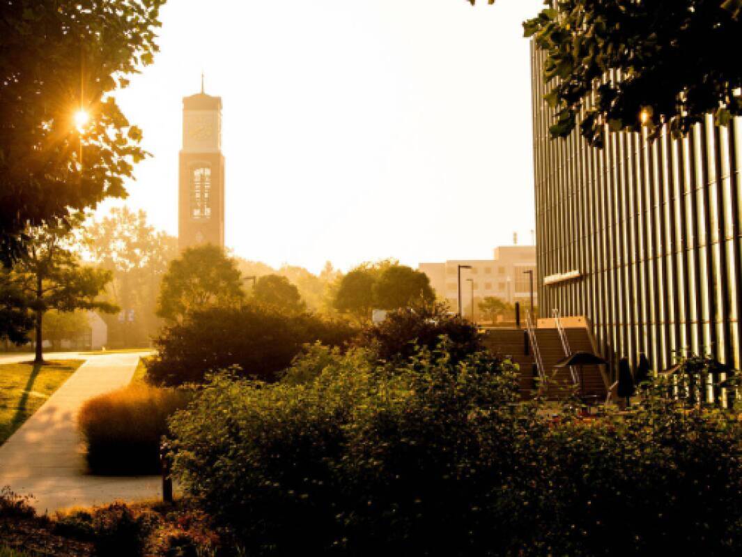 The Mary Idema Pew Library windows reflect the sunrise with the Cook Carillon clock tower in the distance.